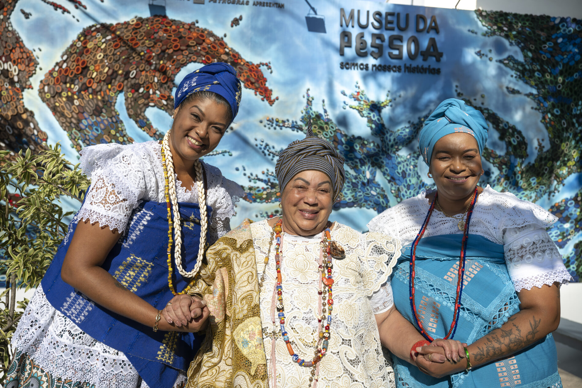 Três mulheres negras, de turbante, estão em frente à nova Fachada do Museu da Pessoa, que remete a um globo, no dia de lançamento da Programação 2025