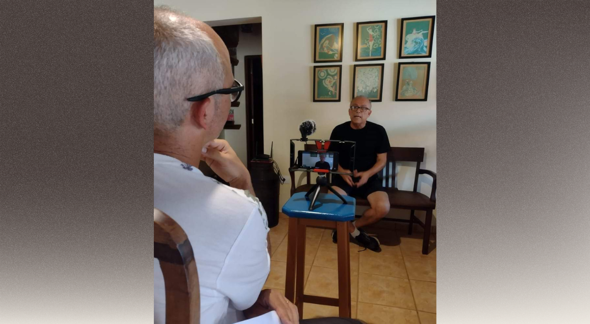 Dois senhores sentados, um em frente ao outro. O que está de costas, tem uma câmera ligada e conduz uma entrevista. Registros do Núcleo Museu da Pessoa Vozes Daqui de Parelheiros.