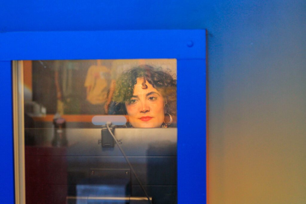 Mulher branca, com os cabelos encaracolados está dentro da cabine do Museu da Pessoa para contar sobre sua experiência com desafios ambientais.