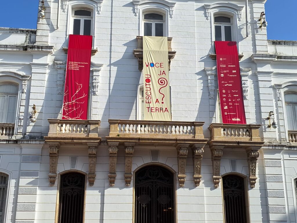 Prédio histórico branco com banner escrito: Você Já Escutou a Terra?