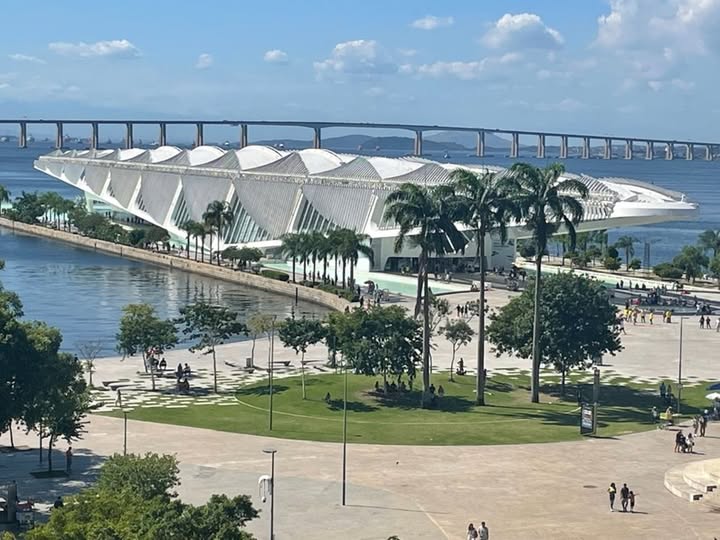 Museu do Amanhã
Gustavo de Castro Praxedes
A primeira vez que fui ao Museu do Amanhã, foi em 2016 quando estava trabalhando nos Jogos Olímpicos do Rio de Janeiro como voluntário. Tudo me parecia grandioso e futurista. Transitar por entre seus 30 mil metros de área, me parecia mesmo uma coisa do futuro. Afinal, você entra no museu para explorar o presente e imaginar como será o futuro.
O prédio, um projeto do arquiteto espanhol Santiago Calatrava, nos faz imaginar, o esqueleto de uma baleia, porém, a ideia do autor, é lembrar a estrutura de uma bromélia e o movimento das asas de um pássaro. O importante é que ao adentrar no museu, as exposições contidas nele, faz o visitante viajar por um mundo real e ao mesmo tempo imaginário. Cada modulo visitado, é uma grande descoberta.
O primeiro modulo, a exposição principal retrata o Cosmos. Nela, é apresentado um filme, em que “traça uma narrativa sobre a formação do universo e da vida na terra com sobreposições de animações digitais e imagens captadas em câmera que causam grande impacto sensorial ao público”, como é informado no site do próprio museu do Amanhã.
No segundo, é a seção Terra. Nela o visitante todo o tempo, se indaga, sobre quem somos. Cada sala é uma nova descoberta.
Na terceira parte, é abordado o Antropoceno, ou seja, a influência humana e os impactos ambientais e sociais, negativos, causados por sobre o planeta.
Na quarta, denominada de “Amanhãs”, fala sobre o mundo e a vida na Terra no futuro, apresentando conceitos como o da hiperconectividade e resgatando a importância da sustentabilidade.
Por fim, na última parte, a exposição principal é o pavilhão 