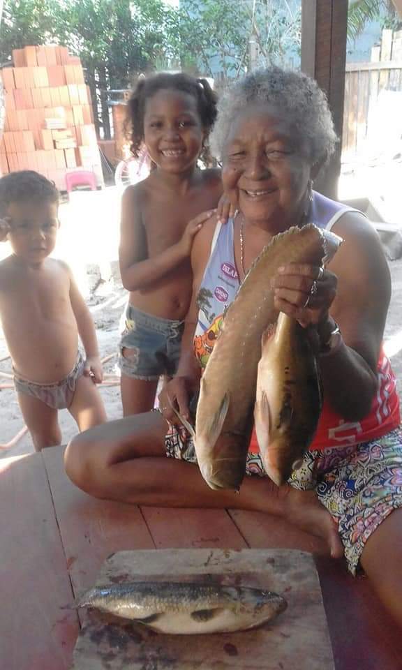NA IMAGEM DONA DIVINA TRATANDO PEIXE AO LADO DE SEUS BISNETOS